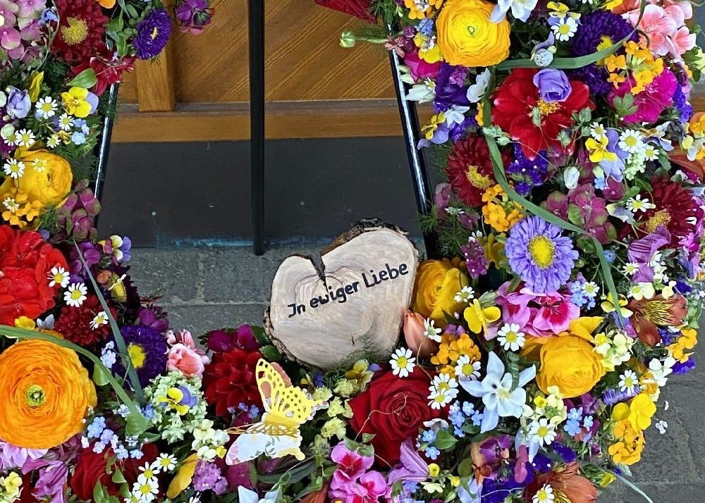 Beschriftetes Herz „In ewiger Liebe“ in einem bunten Trauerkranz