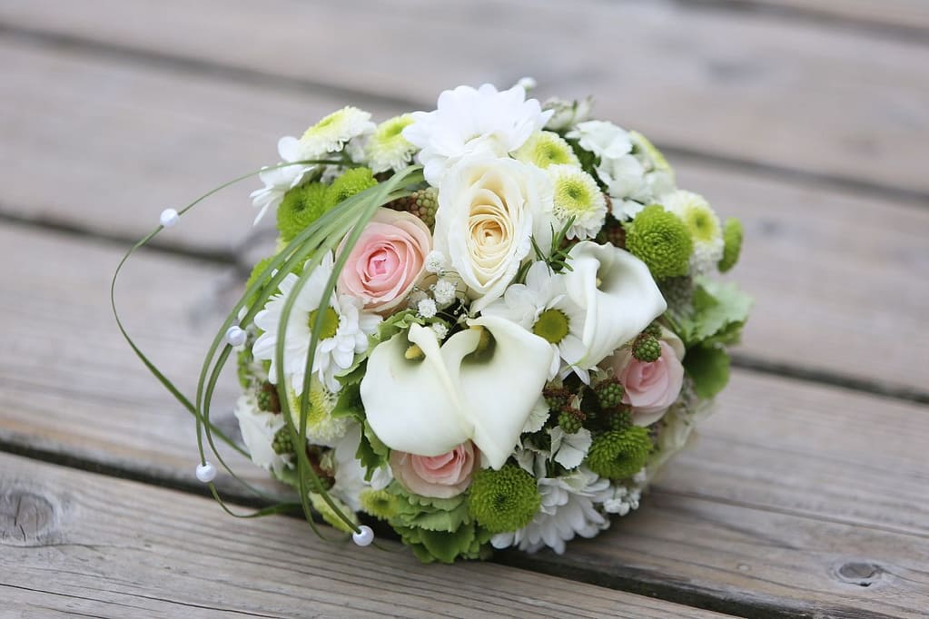 Weißer Brautstrauß mit Callas und Gänseblümchen auf Holzterrasse