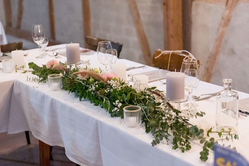 Lange Tafel mit Grün-Girlande und Kerzen in rustikaler Scheune