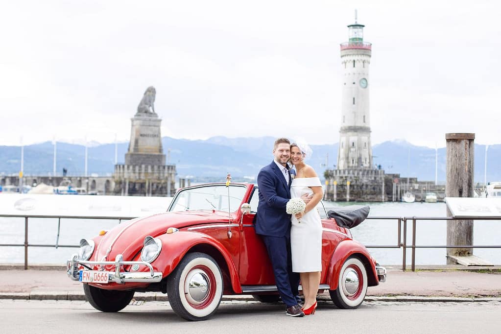 Brautpaar mit rotem VW-Käfer-Cabrio am Lindauer Hafen, Leuchtturm im Hintergrund