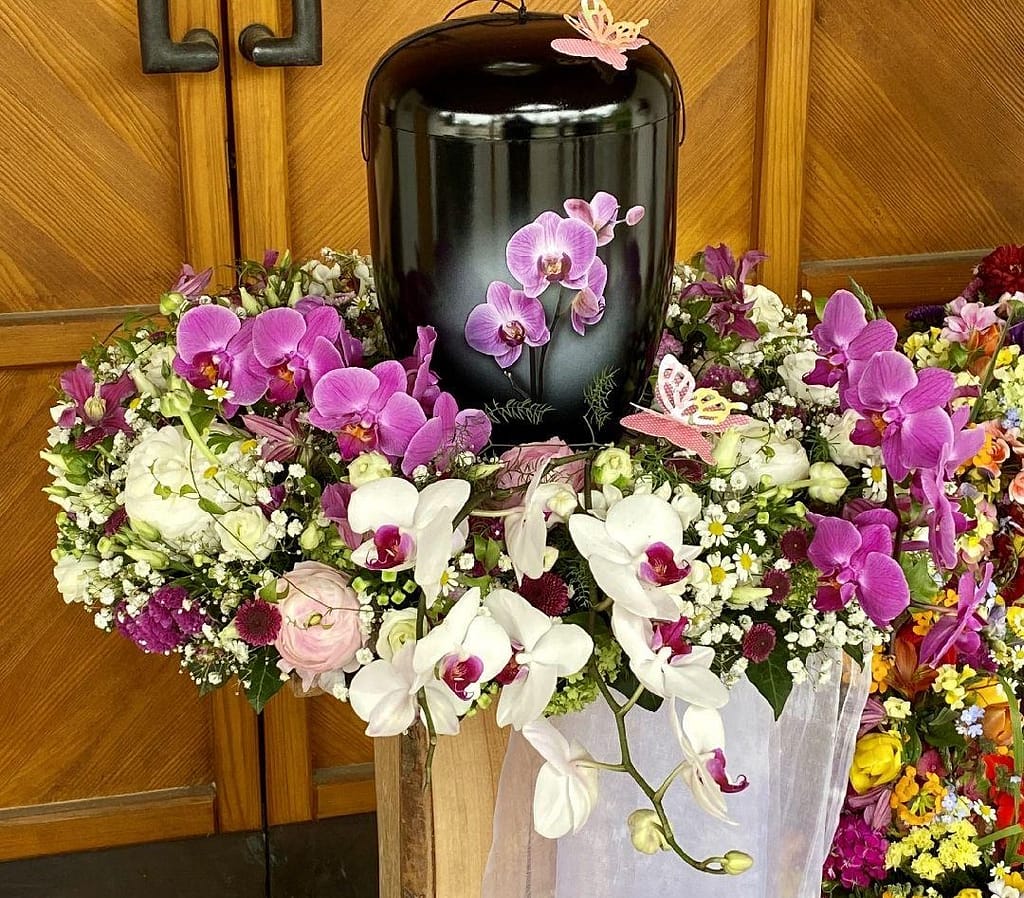 Schwarze Urne mit lila Orchideen und weißem Tuch