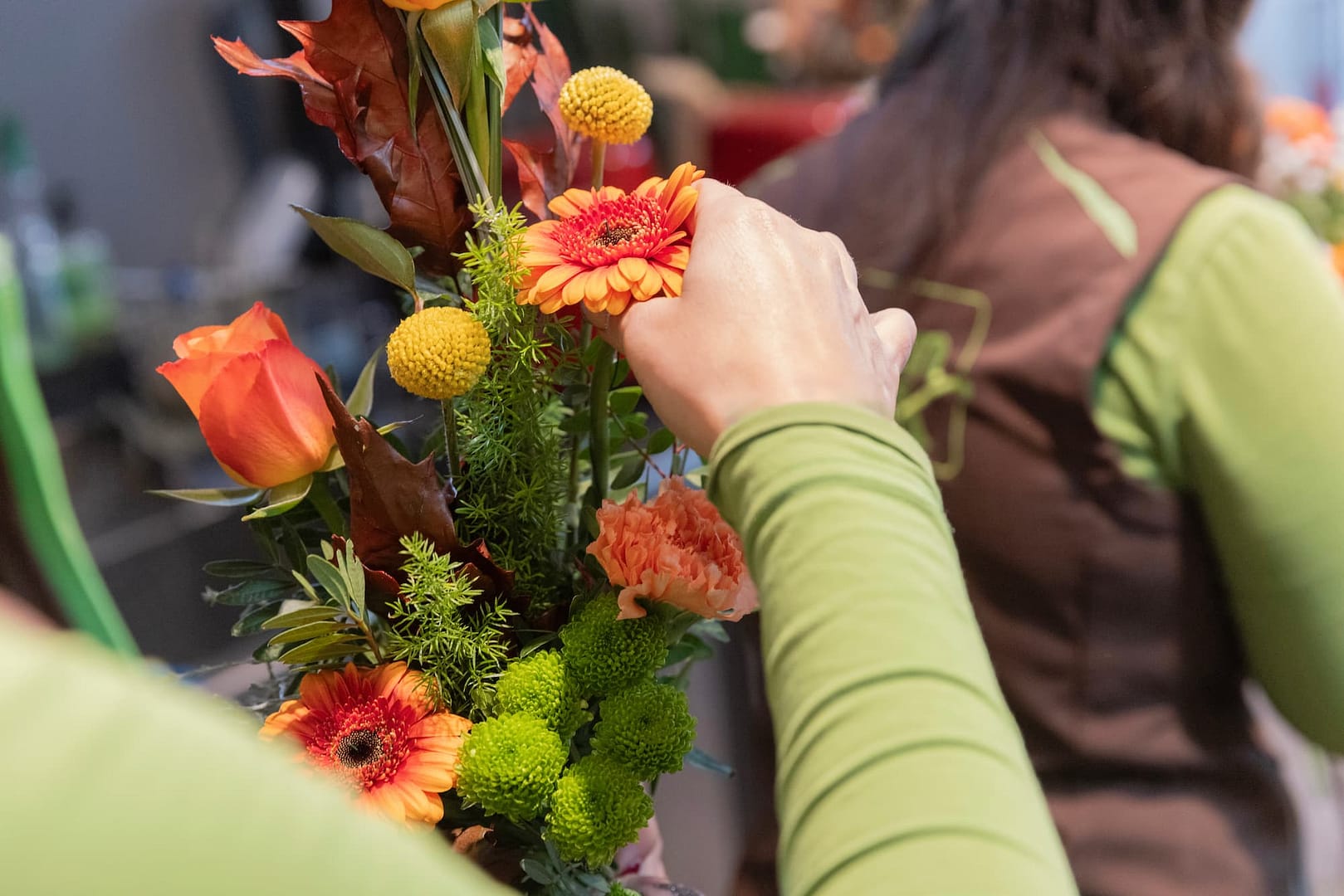 Floristin bindet einen herbstlichen Blumenstrauß mit orangen Gerbera und Rosen