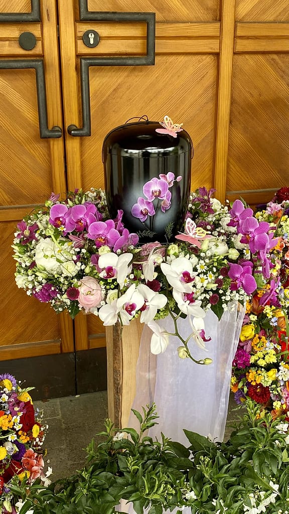 Schwarze Urne mit lila Orchideen und weißem Schleier geschmückt