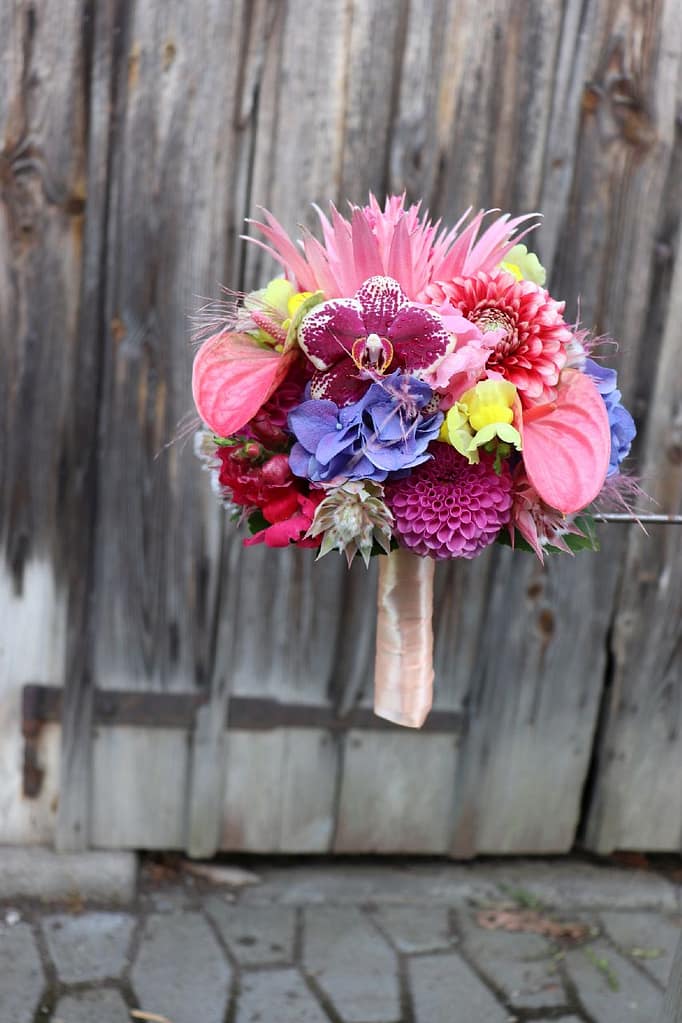 Exotischer Brautstrauß in Pink und Lila mit Orchidee vor Holztor