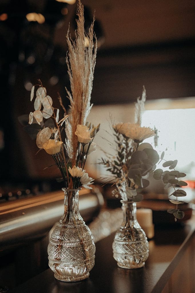 Zwei Glasvasen mit Pampasgras und Trockenblumen auf dunkler Ablage