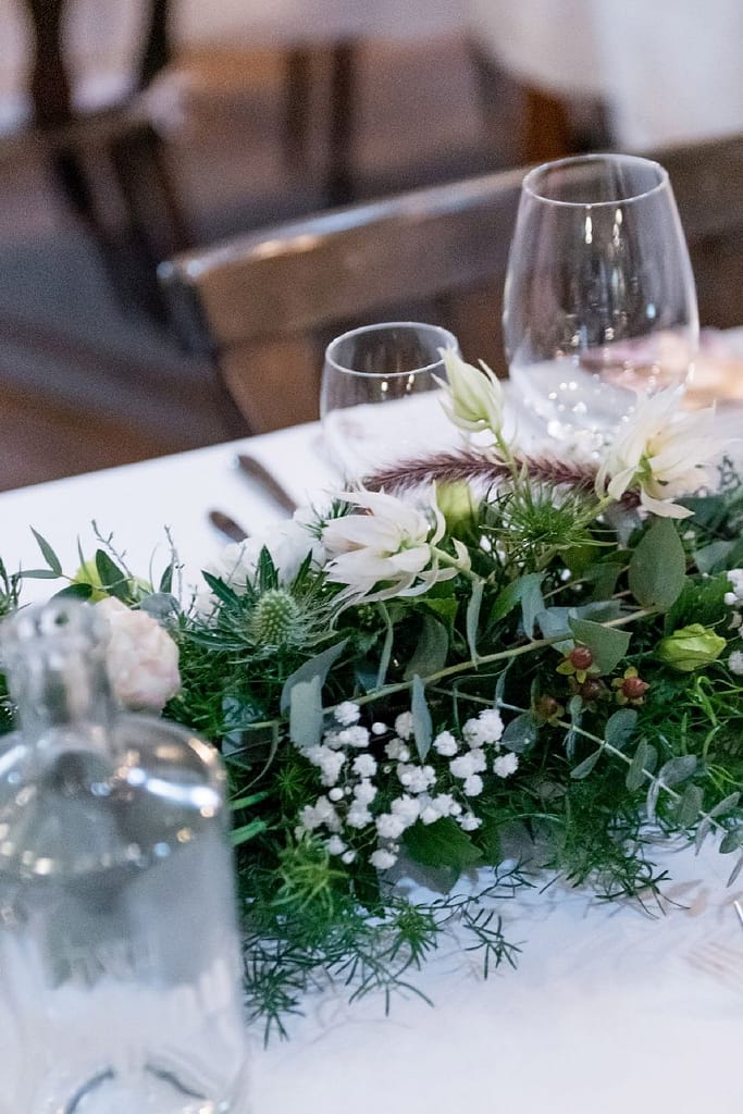 Tischgesteck mit weißen Blüten und Weingläsern, Nahaufnahme