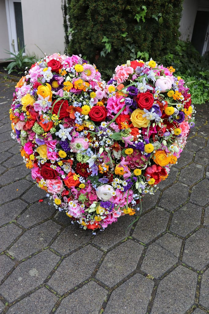 Herzförmiges buntes Trauergesteck mit Rosen und Ranunkeln