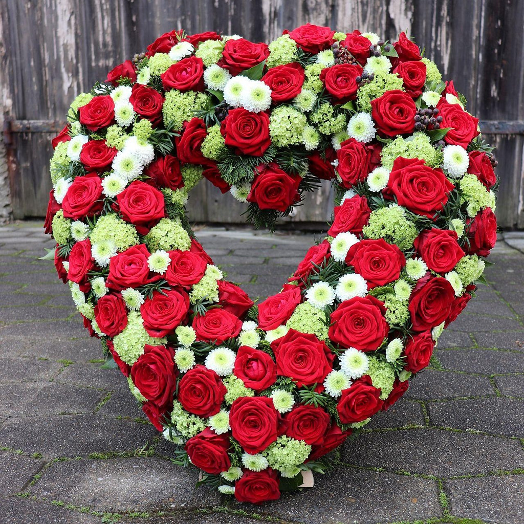 Offenes Trauerherz aus roten Rosen mit weißen Blüten