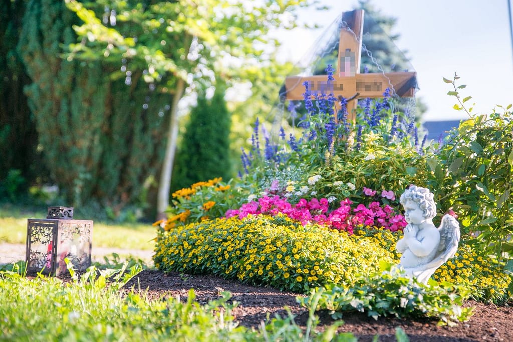 Grabbepflanzung mit bunten Sommerblumen, Engelsfigur und Laterne