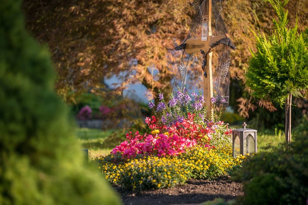 Herbstliche Grabbepflanzung mit rosa und gelben Blumen am Grabkreuz